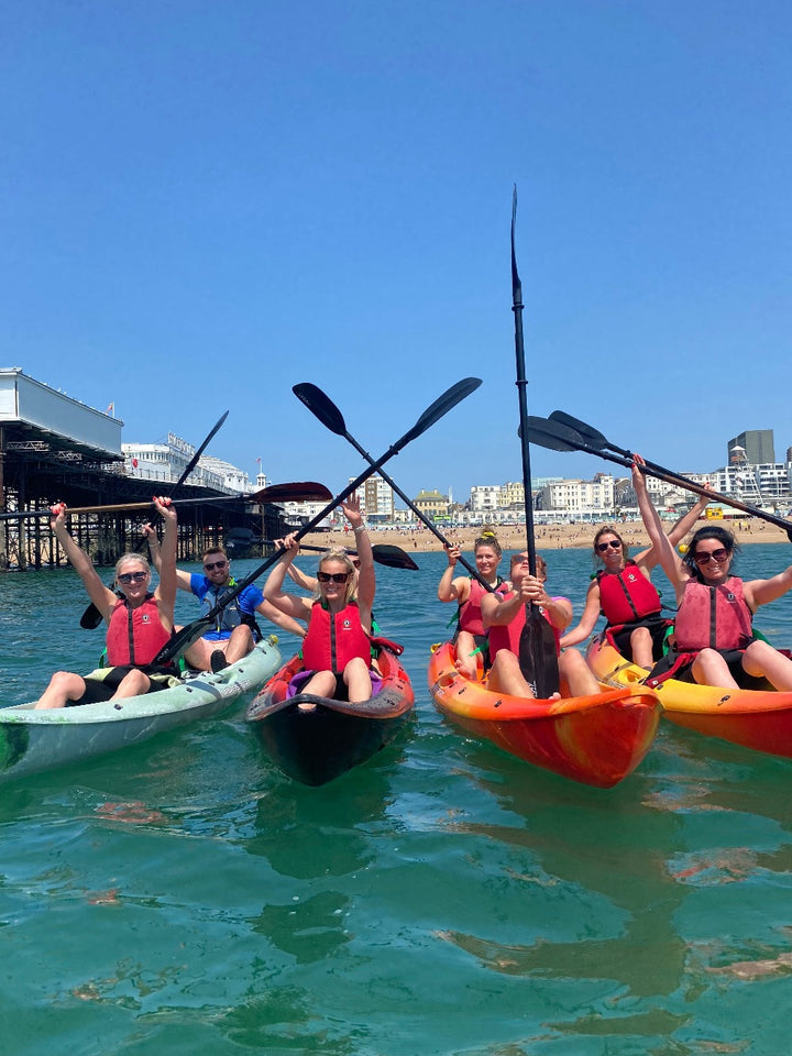 Kayak group on Brighton sea with paddles in air