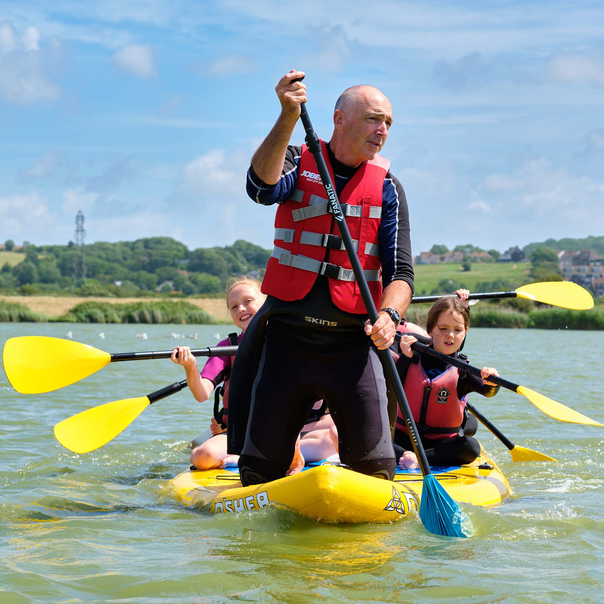 group on jumbo paddleboard with man at front and kids behind