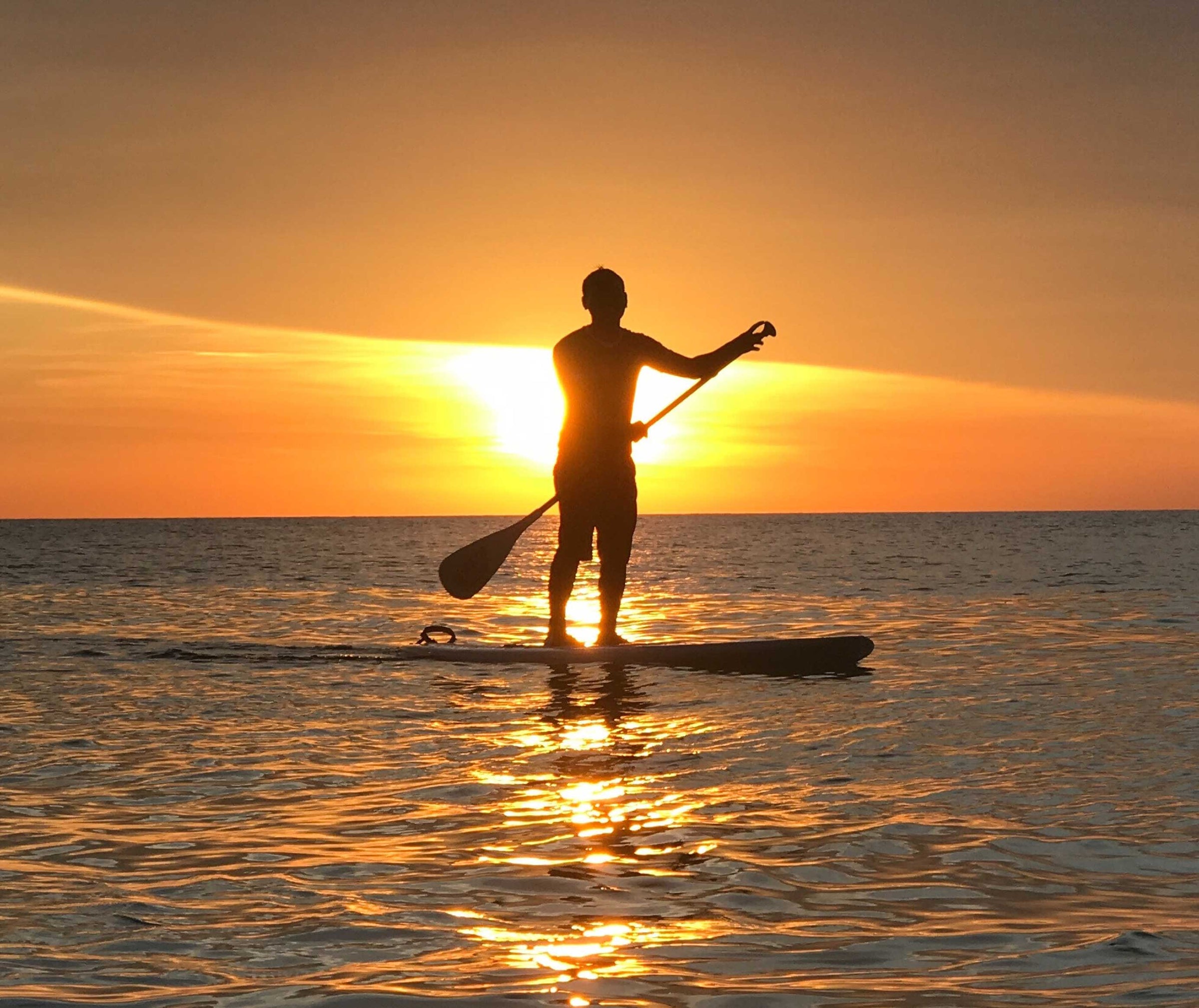 silhouette of man on SUP board in sea during sunset