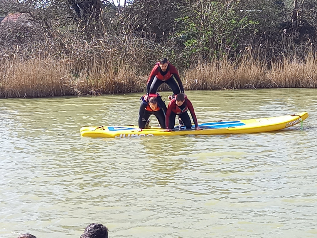 Three men doing a human pyramid on jumbo sup on lake