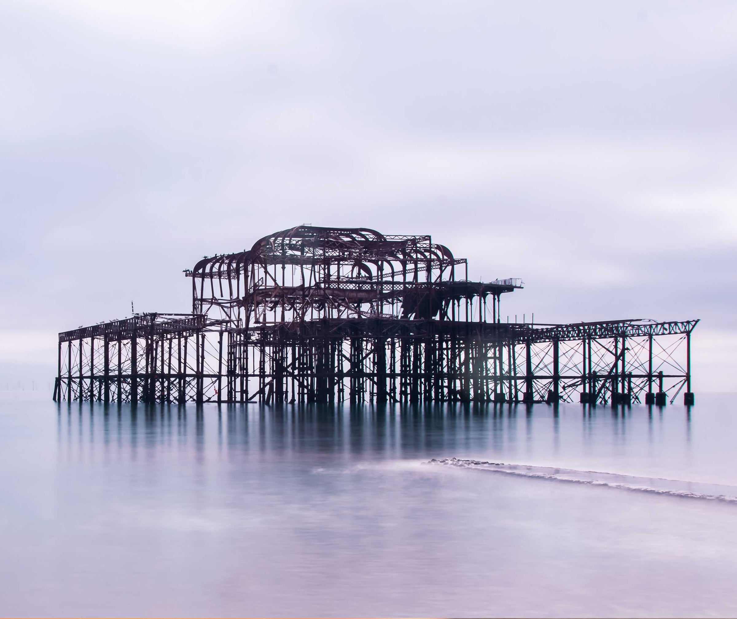 Ruins of brighton west pier structure standing over calm sea water under a soft cloudy sk