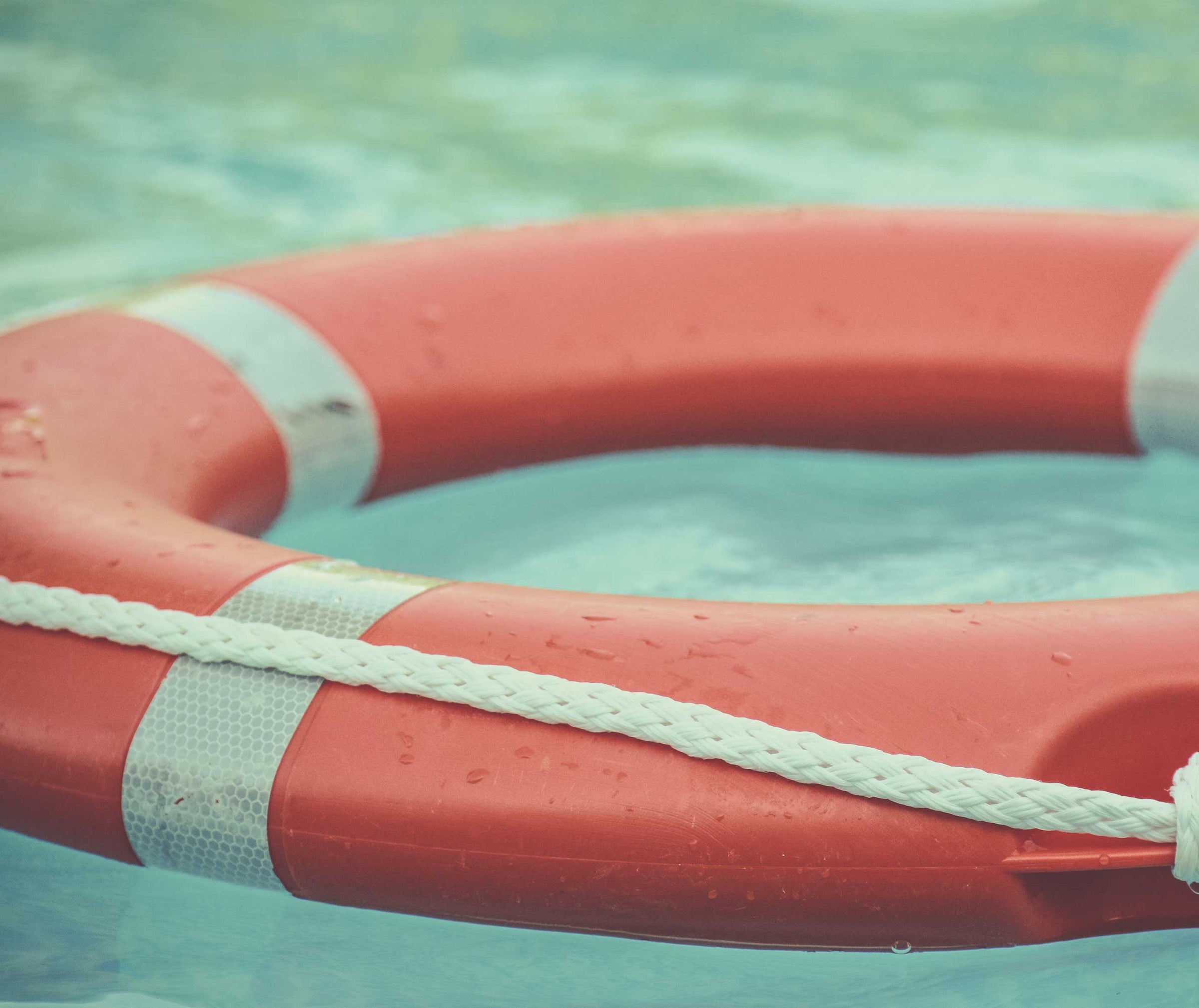 Close-up of a red and white lifebuoy floating on clear blue water for water safety and rescue readiness.